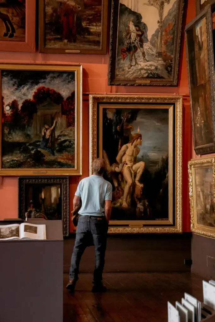 Man stands observing classic paintings in a Paris museum art gallery.