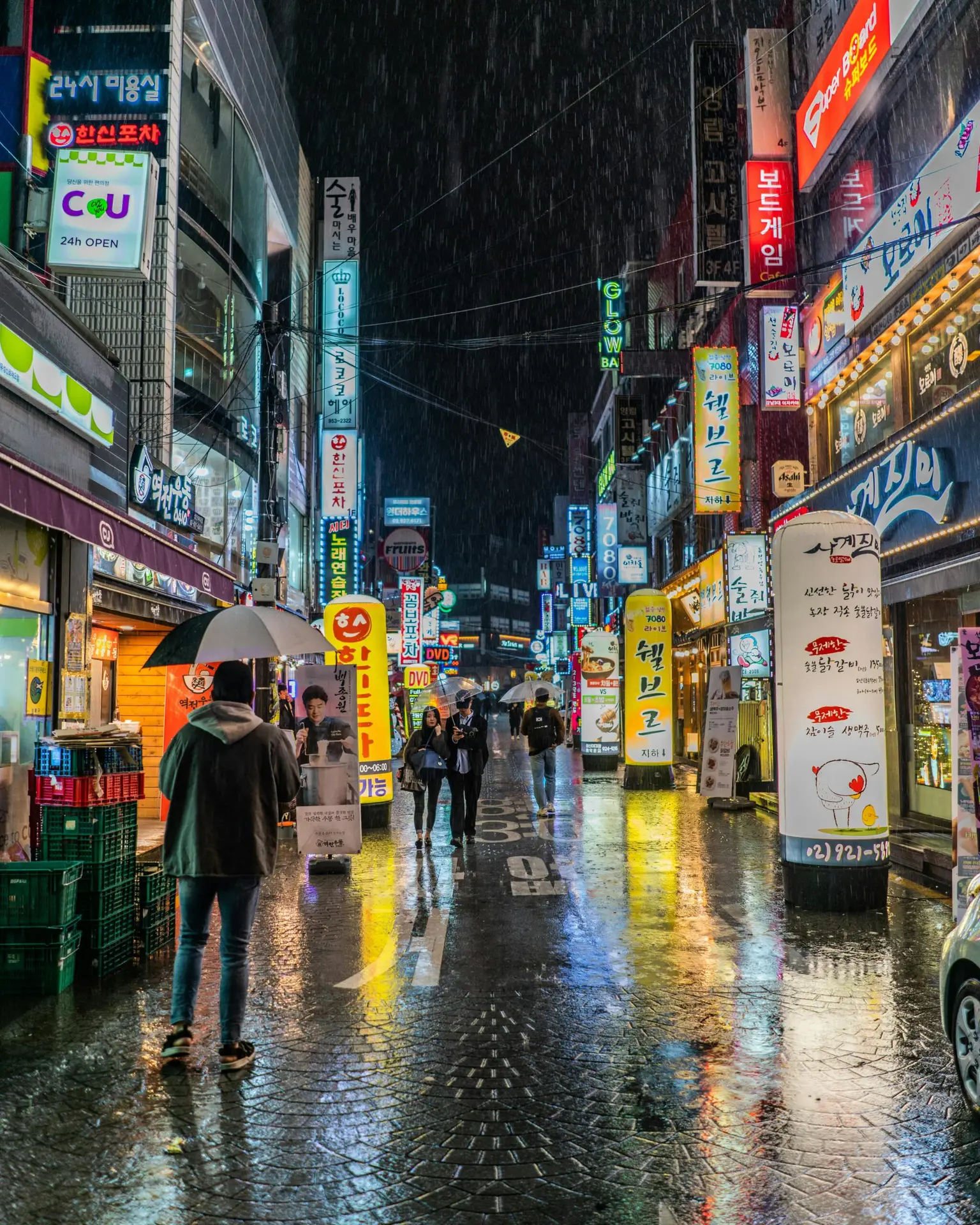 Suad Design Studio A street lit with colorful neon lights In Seoul, South Korea, it showcases the vibrant nightlife with light reflections on the wet pavement.